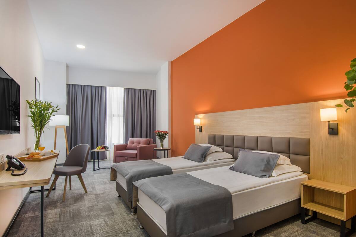 Habitación de hotel con dos camas, un escritorio, una silla y un televisor.