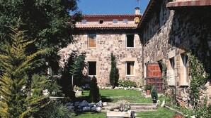 Un edificio de piedra con techo de tejas, un jardín con un banco y un perro acostado sobre el césped.