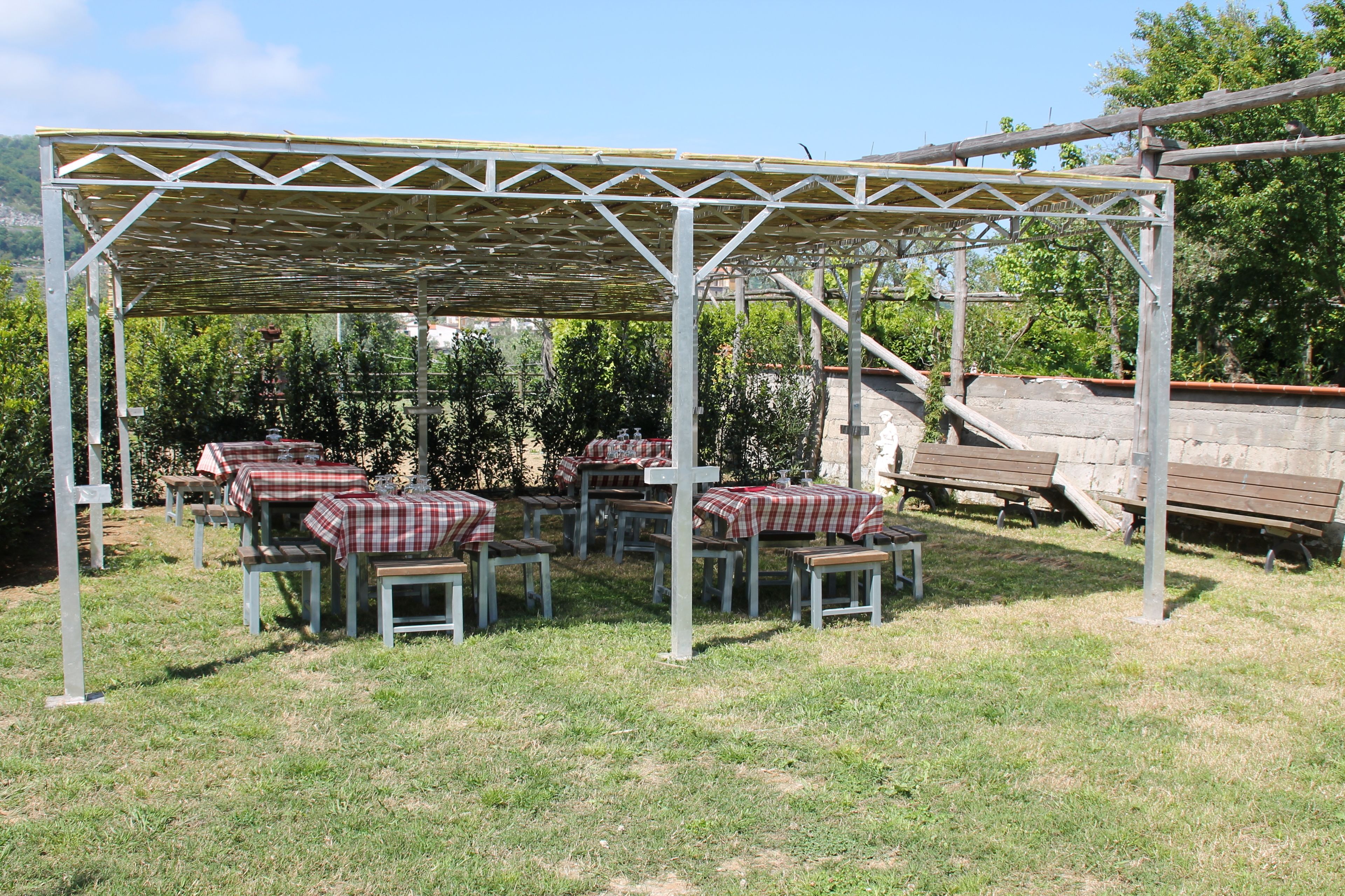 Et udendørs opholdsområde med borde og bænke under en pergola.