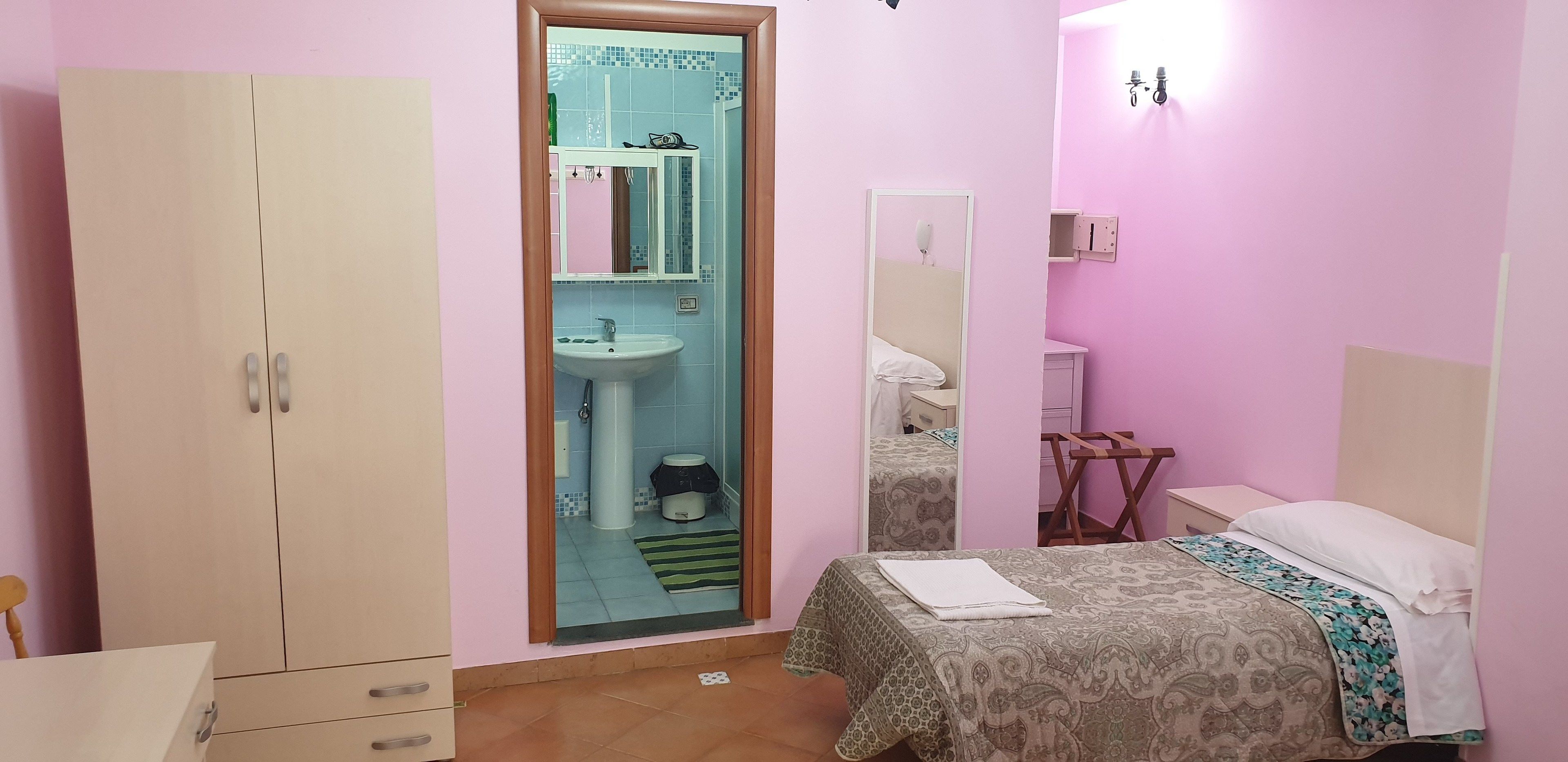 Un dormitorio con cama, armario, espejo, lavamanos y una pequeña mesa.