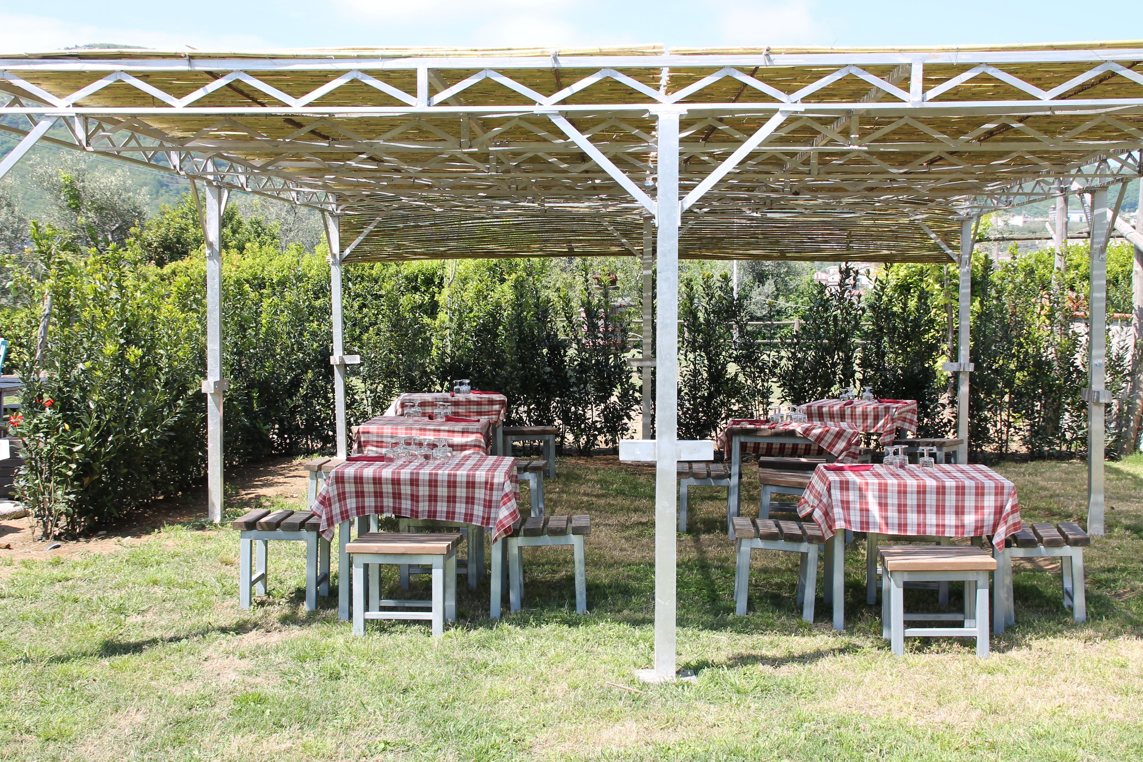 An outdoor patio with tables and benches, covered by a wooden pergola.