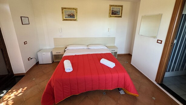 Ein Hotelzimmer mit einem Bett, zwei Nachttischen, einem Wandspiegel und zwei gerahmten Bildern.