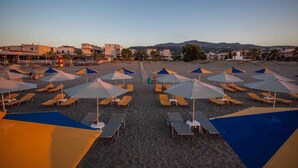 Ein Strand mit Reihen von Liegestühlen und Sonnenschirmen, einem klaren Himmel und Gebäuden im Hintergrund.
