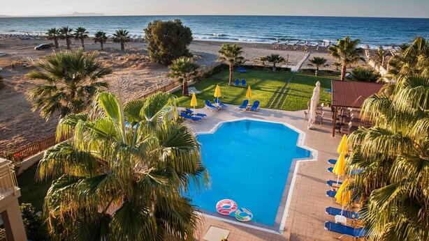 Ein Pool mit Liegestühlen und Sonnenschirmen, umgeben von Palmen und Blick auf Strand und Meer.