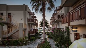 Ein Innenhof mit einer Palme, einem Wasserspiel und einer Bank. Gebäude mit Balkonen und ein Schild mit der Aufschrift "LIAN BEACH".