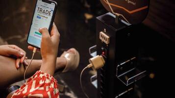 A person using a mobile device at a charging station with a sign that reads "Trade Recharge your cellphone here."