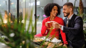A couple seated at a table with a glass of beer, surrounded by indoor plants and a modern interior. - Trade Hotel (Juiz de Fora)