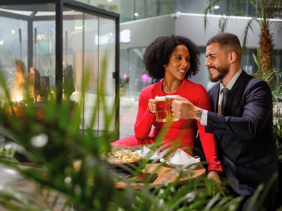 Um casal sentado à mesa com uma cerveja, cercado por plantas e um interior moderno.