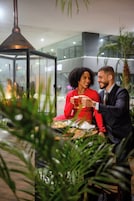 A couple seated at a table with a glass of beer, surrounded by indoor plants and a modern interior.