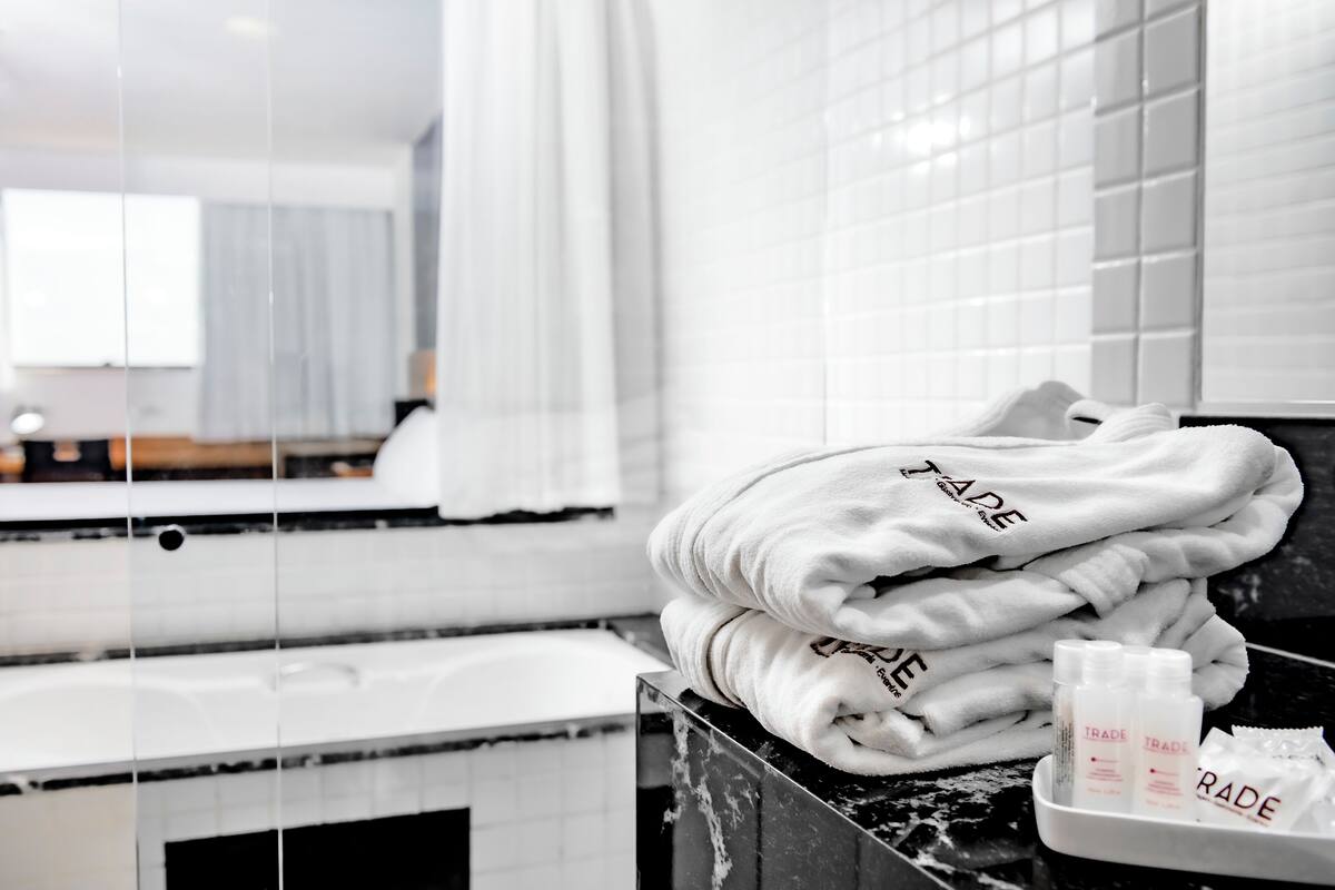 A bathroom with white tiles, a mirror, and a stack of towels with the word "TRAD" on them.