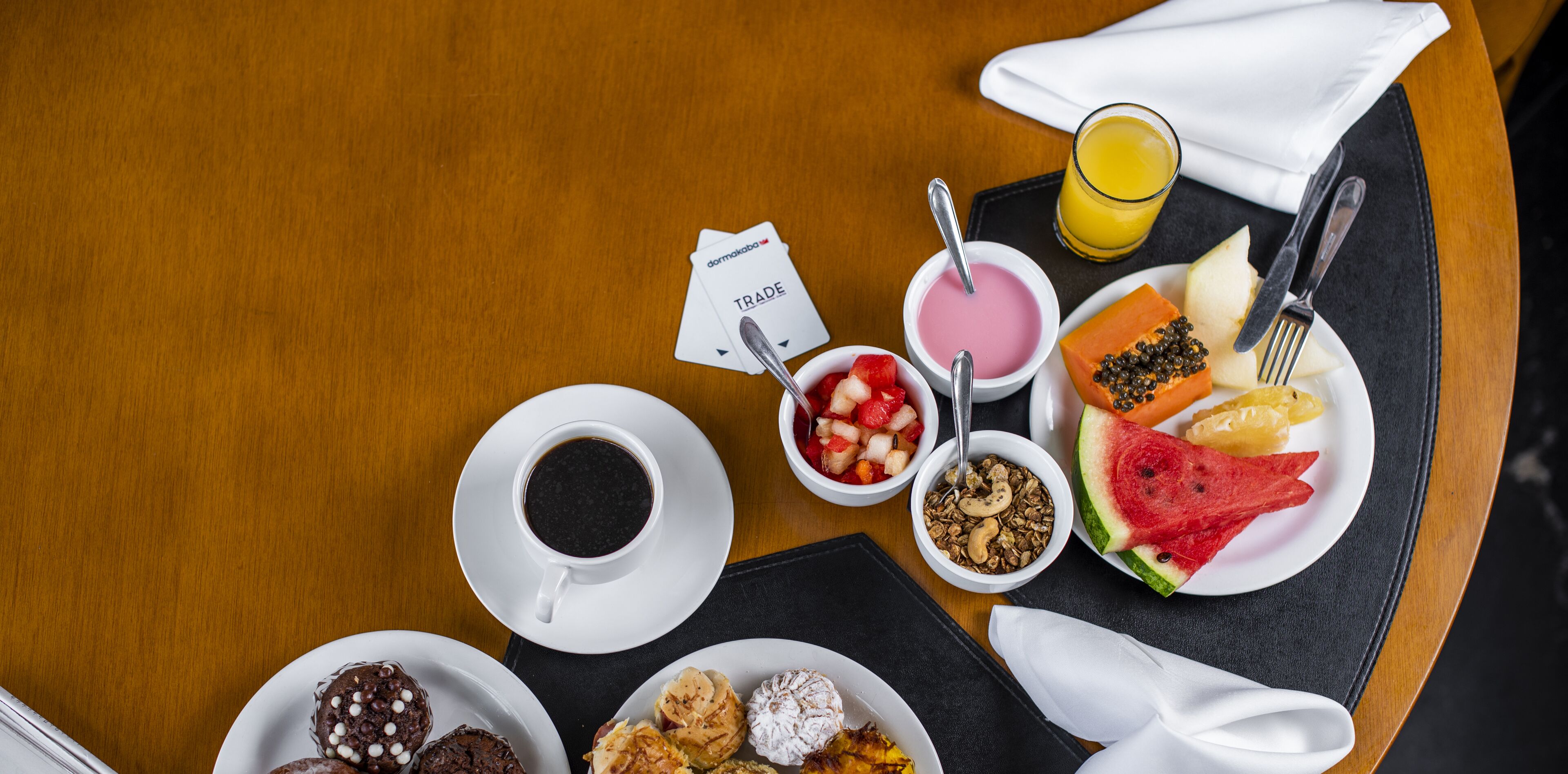 Ein Frühstückstisch mit verschiedenen Speisen, darunter Kaffee, Joghurt, Müsli und Obst.