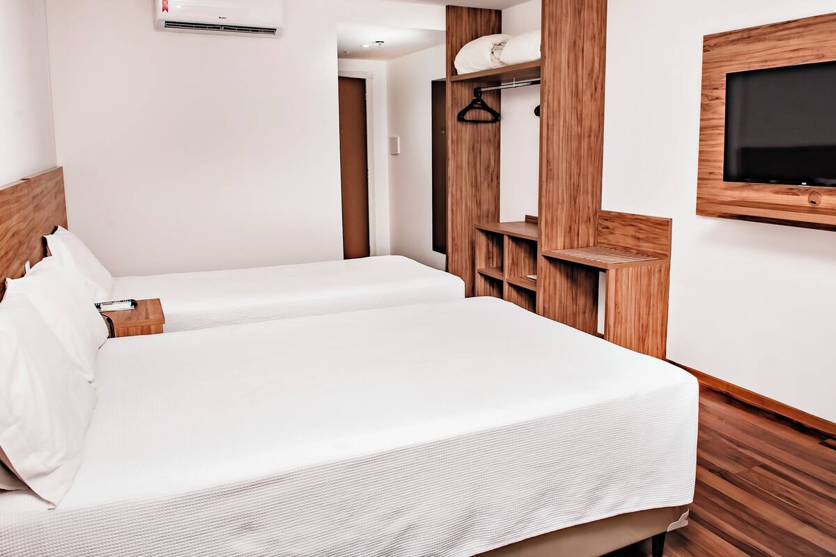 A neatly arranged hotel room with a bed, a TV mounted on the wall, and a wooden wardrobe.