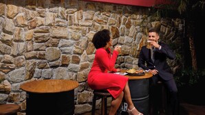 Two people seated at a table in a room with a stone wall and a 'TRADE' sign. - Trade Hotel (Juiz de Fora)