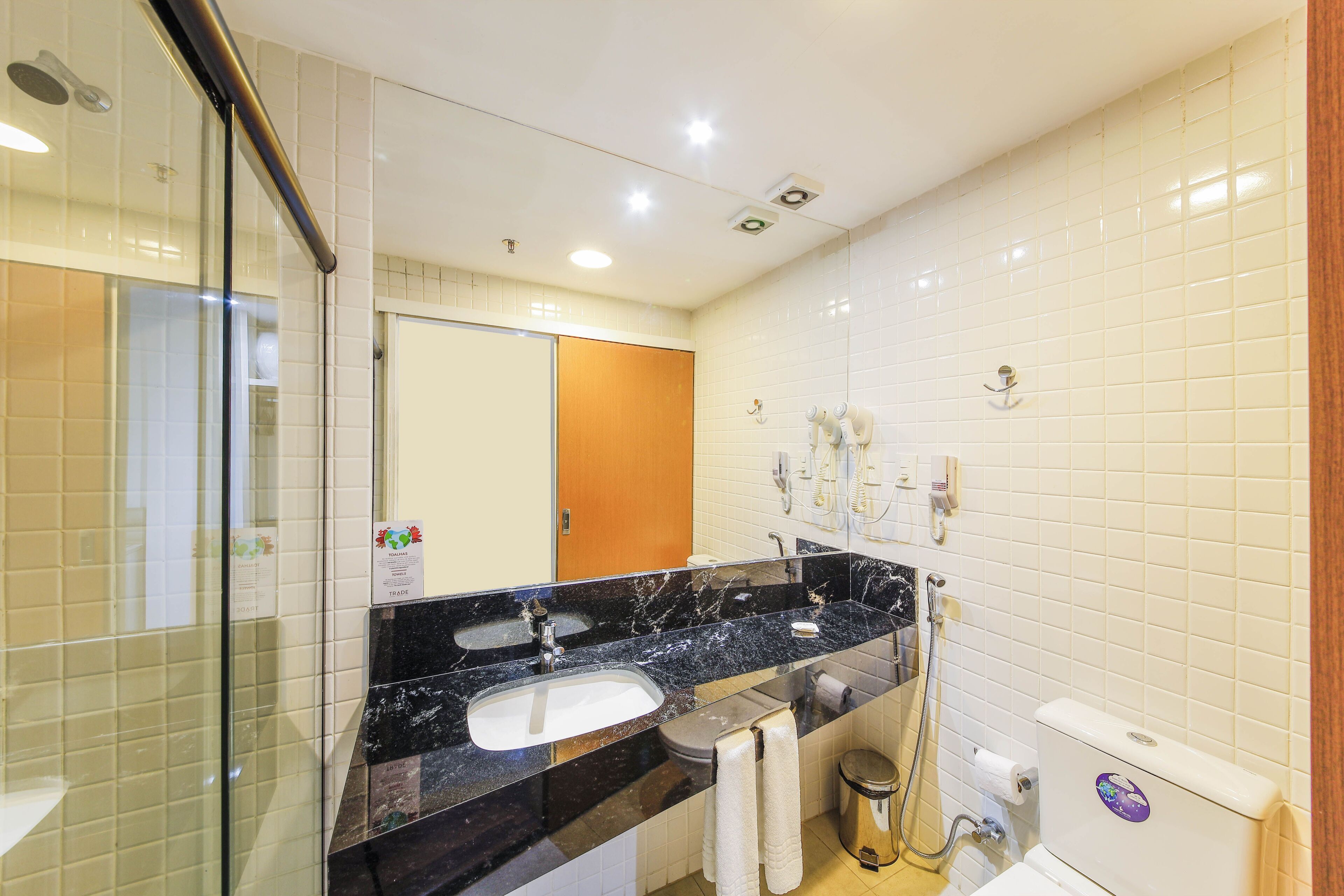 Un bany modern amb un lavabo de marbre negre, una dutxera amb envàs de vidre i parets revestides de rajoles blanques.