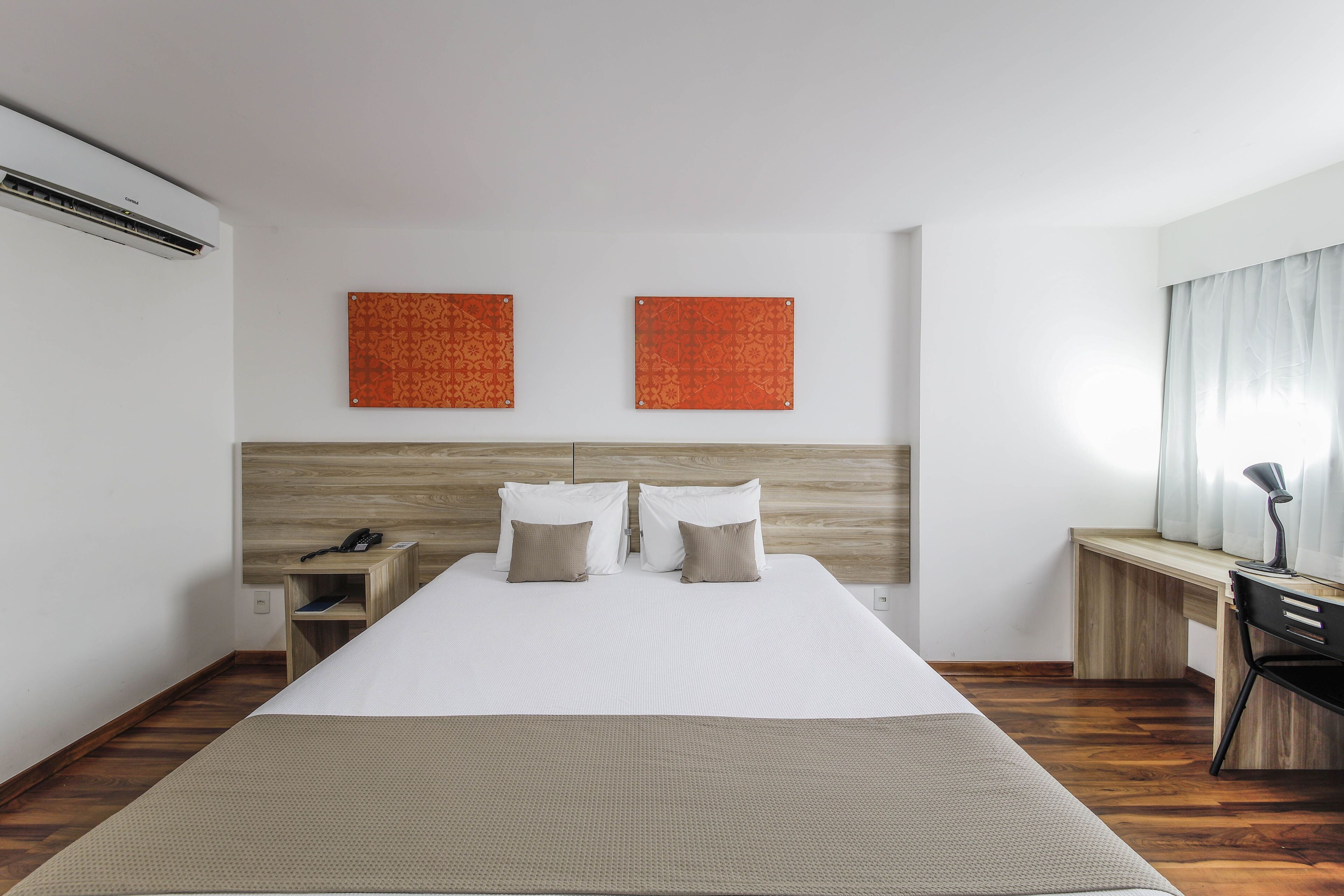 A hotel room with a bed, bedside table, lamp, and two wall-mounted artworks.