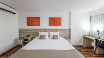 A hotel room with a bed, bedside table, lamp, and two wall-mounted artworks.