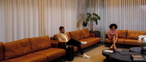 A modern living room with brown leather sofas, a coffee table, and a large potted plant.
