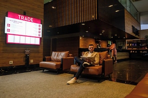 A modern lobby with leather seating, a digital signboard, and a bar area. - Trade Hotel (Juiz de Fora)