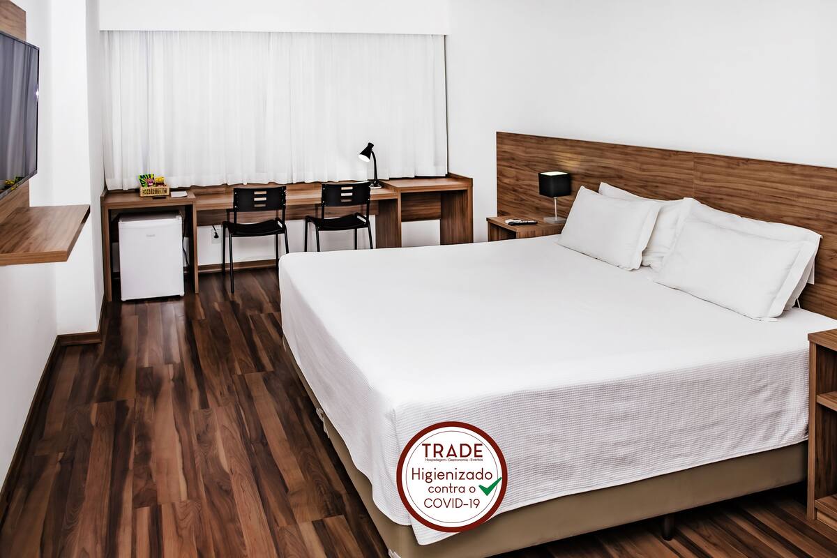 A hotel room with a bed, desk, chairs, and a small refrigerator.