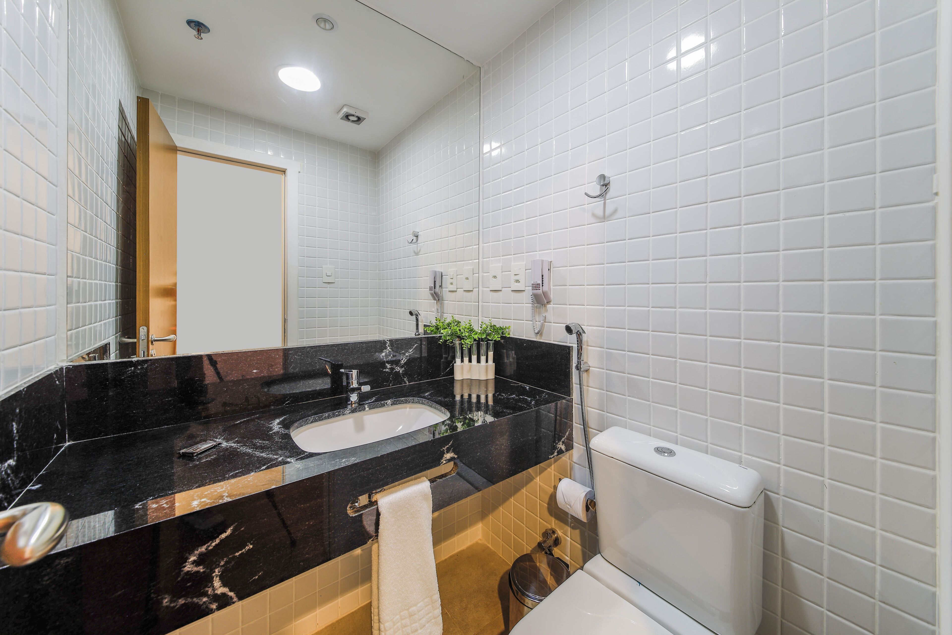 Um banheiro moderno com pia de mármore preto, azulejos brancos, vaso sanitário e chuveiro.