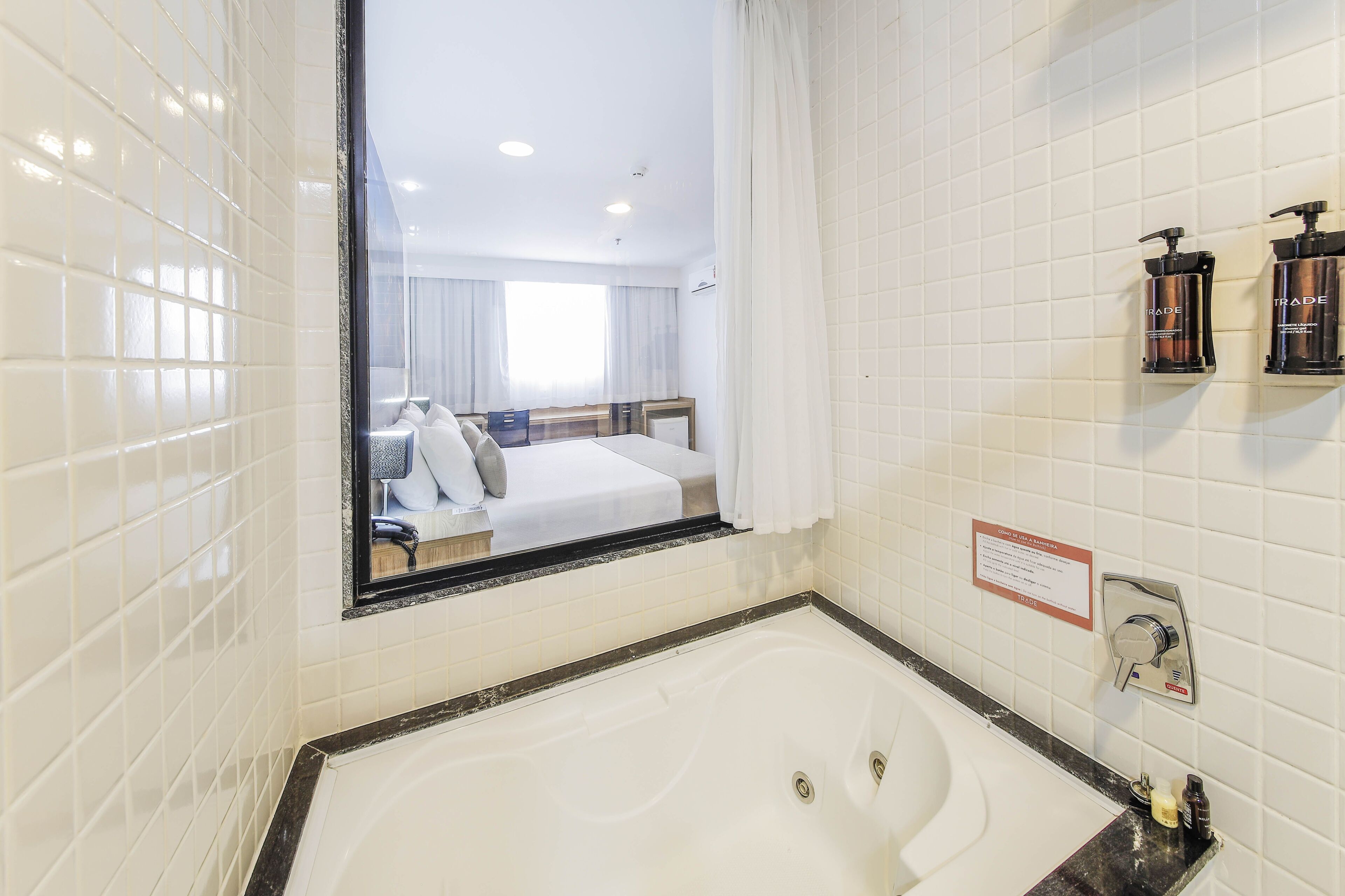 Baño de hotel con un espejo grande, una bañera y artículos de aseo en la pared.