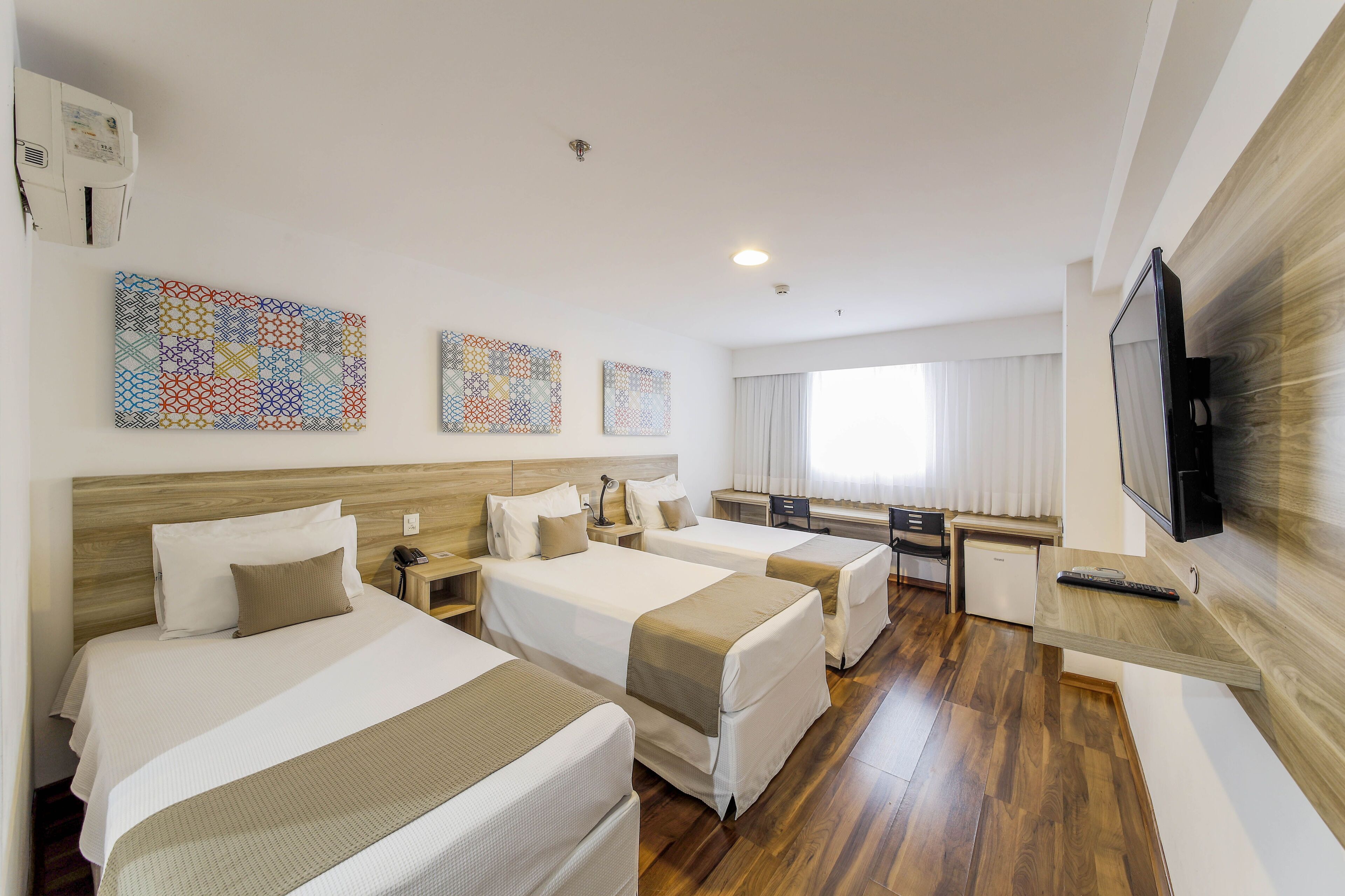 A hotel room with two beds, a desk, a television, and artwork on the wall.