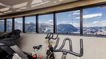 A gym with exercise bikes and treadmills, large windows with a city view.