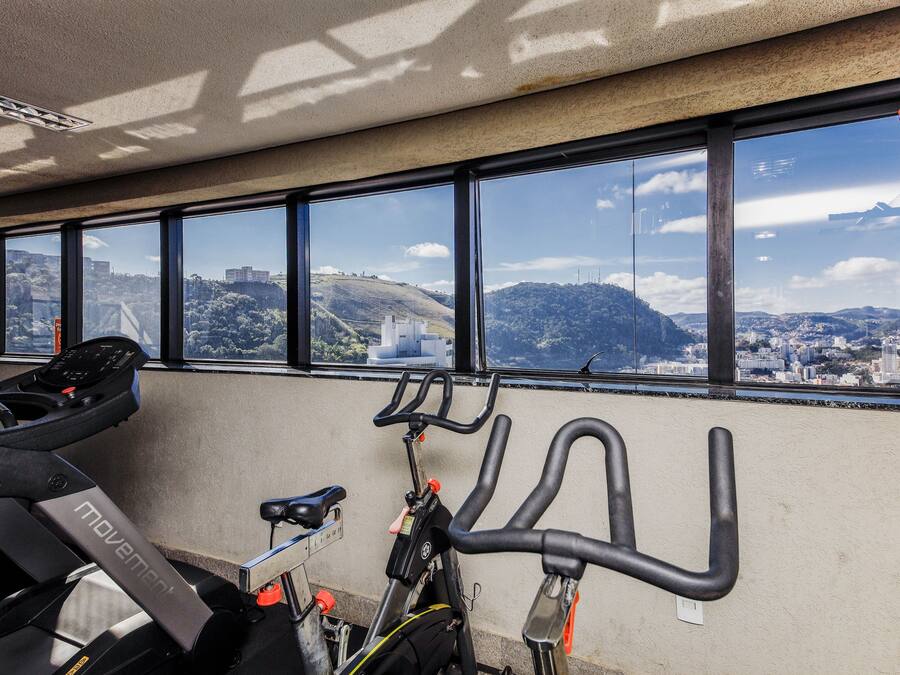 A gym with exercise bikes and treadmills, large windows with a city view.