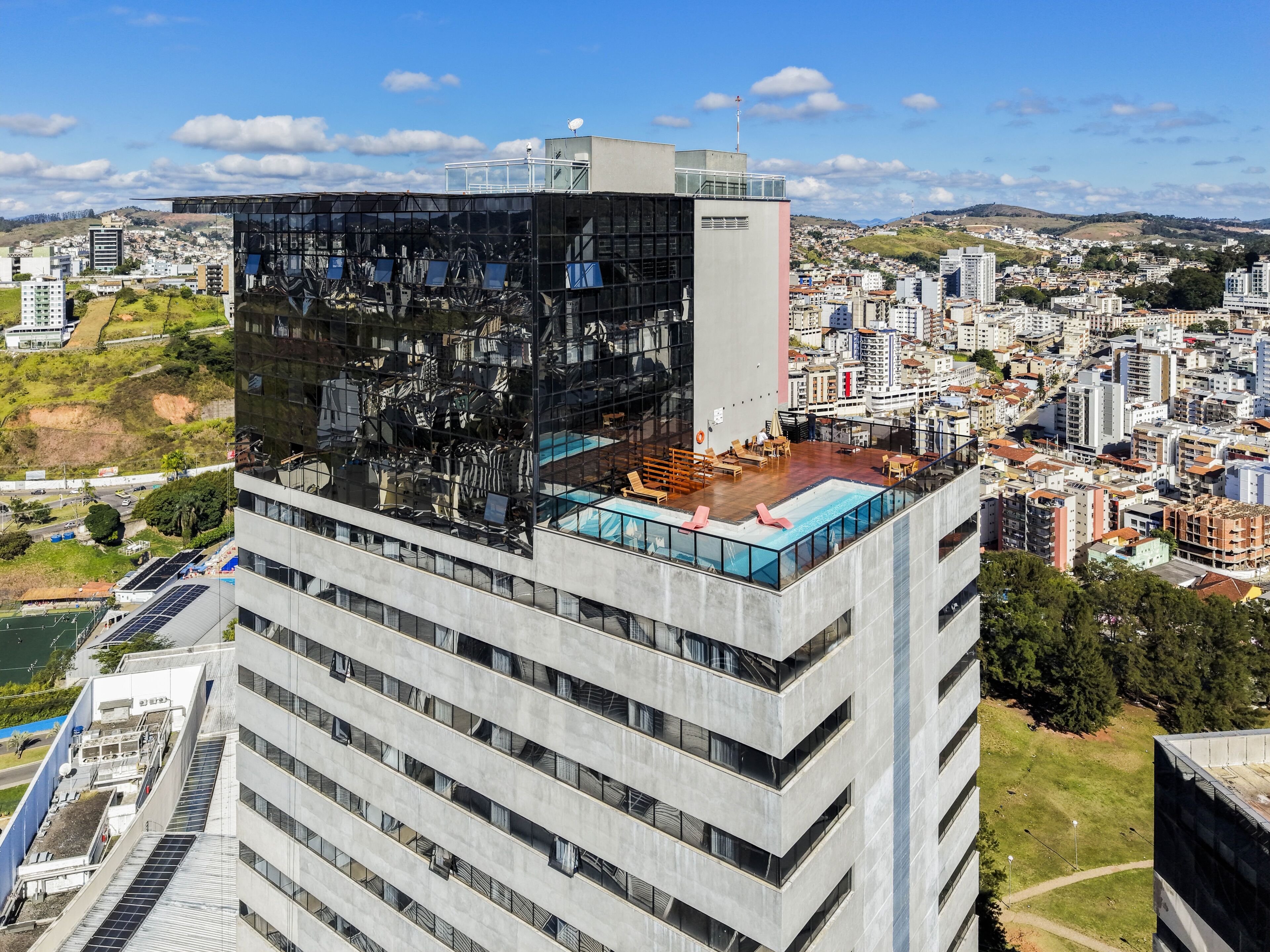 A high-rise building with a rooftop pool and lounge area, surrounded by a cityscape.