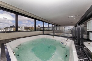Uma banheira de hidromassagem grande e coberta, com vista para a cidade, divisória de vidro e design de interiores moderno.