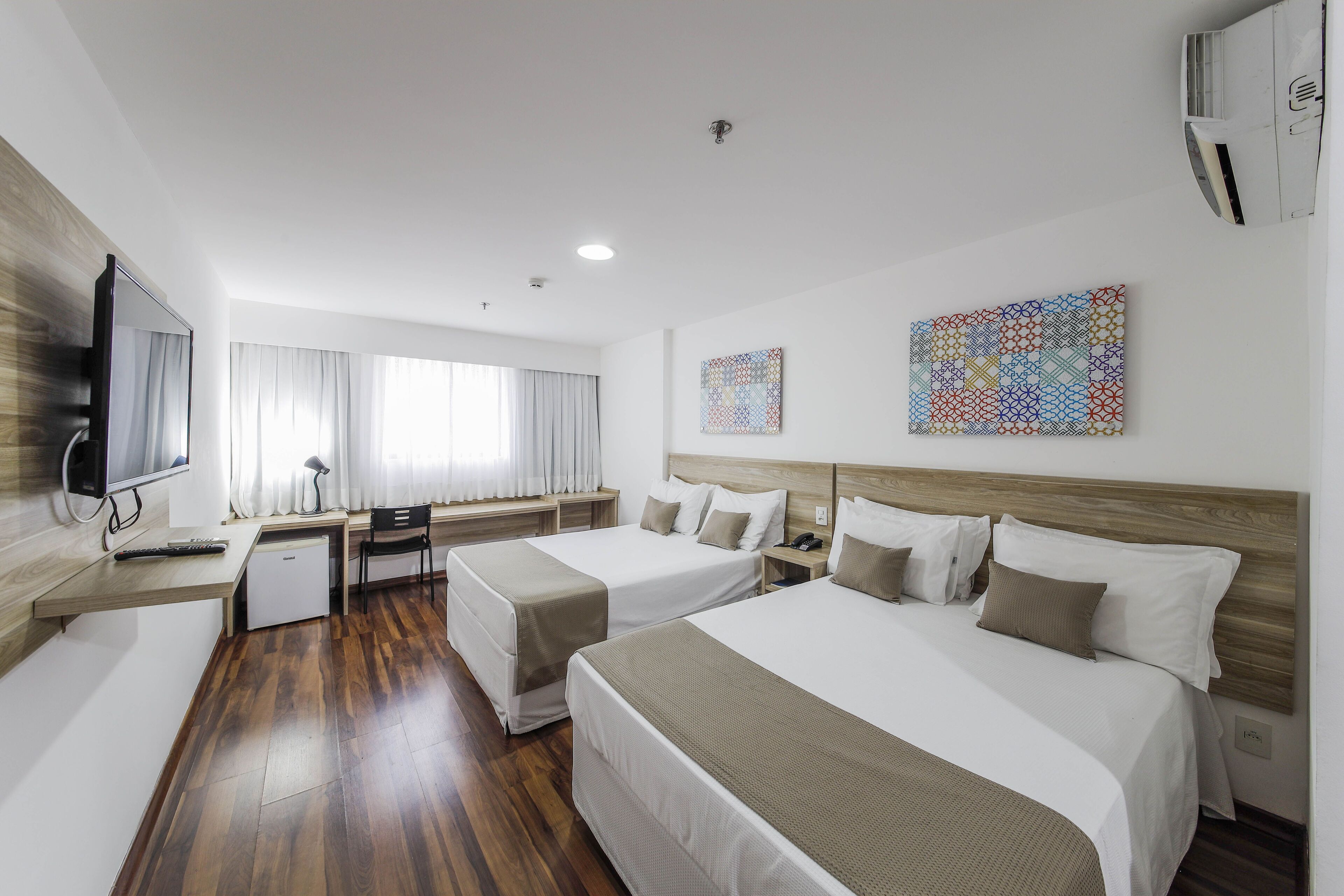 Una habitació d'hotel amb dos llits, una taula de treball, una televisió i obres d'art a les parets.