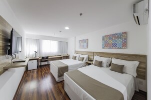 Quarto de hotel com duas camas, uma escrivaninha, televisão e obras de arte nas paredes.