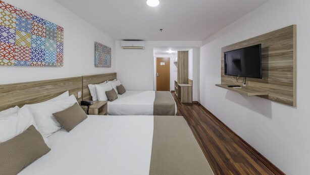 A hotel room with two beds, a TV mounted on the wall, and a wooden floor. - Trade Hotel (Juiz de Fora)