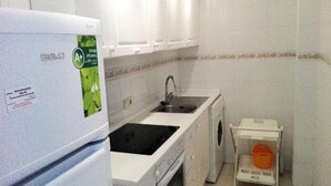 Een functionele keuken met een koelkast, een spoelbak en een kleine wasmachine.