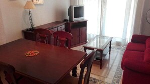Een eethoek met een houten tafel en stoelen, een televisie op een kast, en een rode bank.
