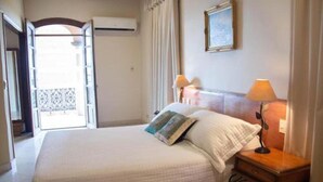 A hotel room with a bed, bedside lamps, a window with curtains, and a wall-mounted air conditioner. - Asuncion House (Asunción)