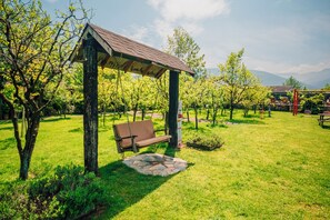 Ein Gazebo mit einer Bank, umgeben von einer grünen Wiese mit Bäumen und einem Kiesweg.