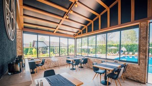 Un restaurant doté d’une terrasse, de grandes fenêtres et offrant une vue sur une piscine.