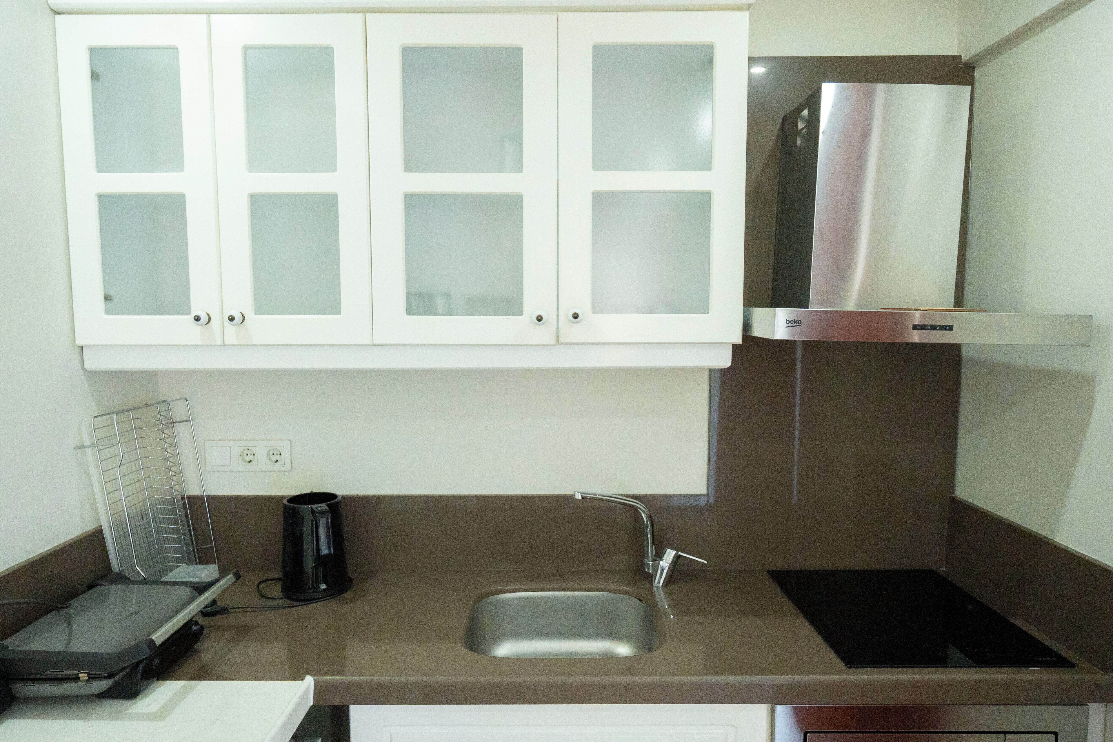 Una cocina con armarios blancos, una campana de acero inoxidable, un fregadero y una cafetera.