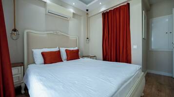 A neatly made bed with white and red bedding, a bedside table, an air conditioning unit, and a wardrobe in a hotel room.
