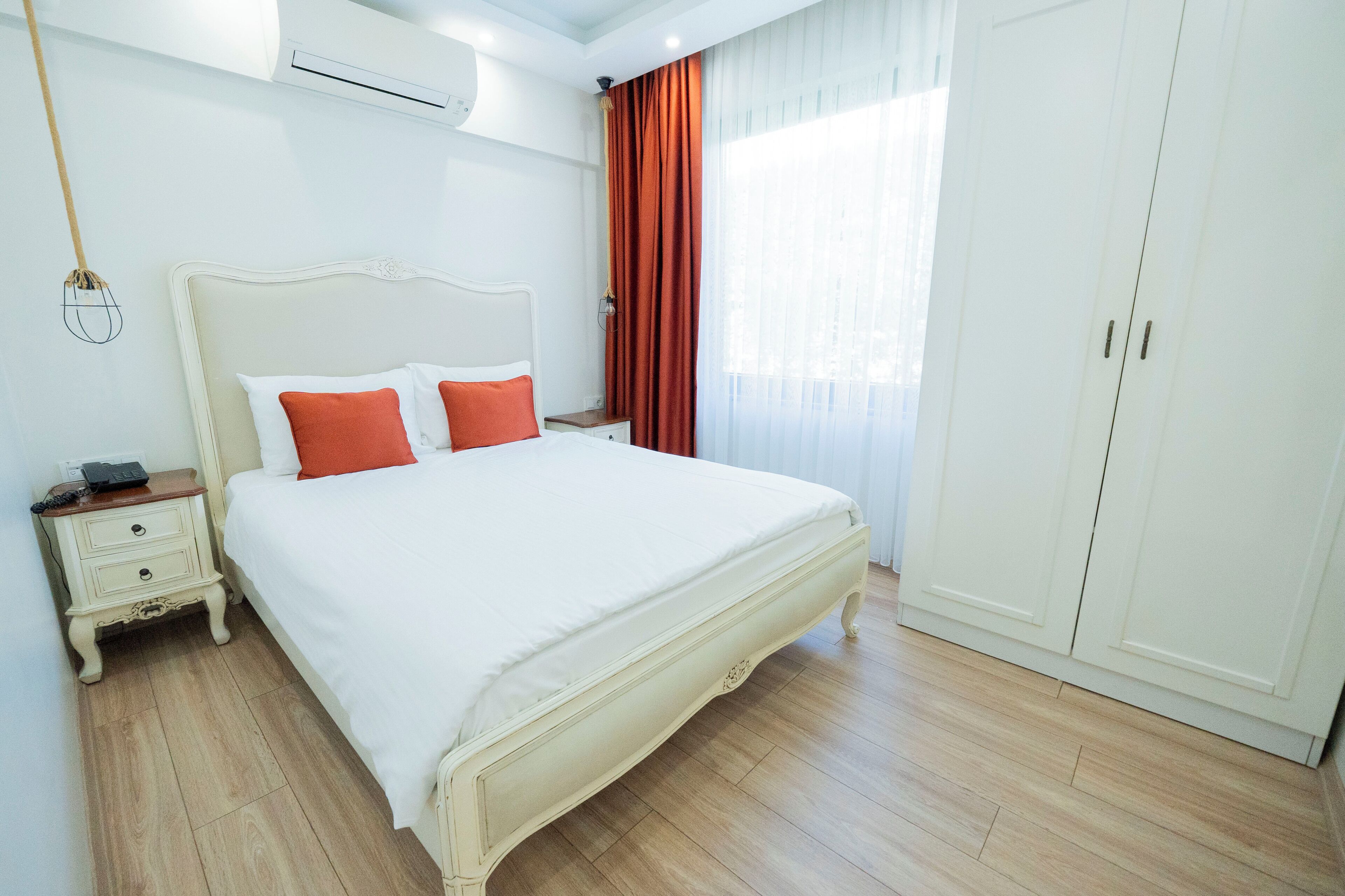 Une chambre bien rangée, avec un grand lit, une table de chevet, une armoire et un luminaire suspendu.