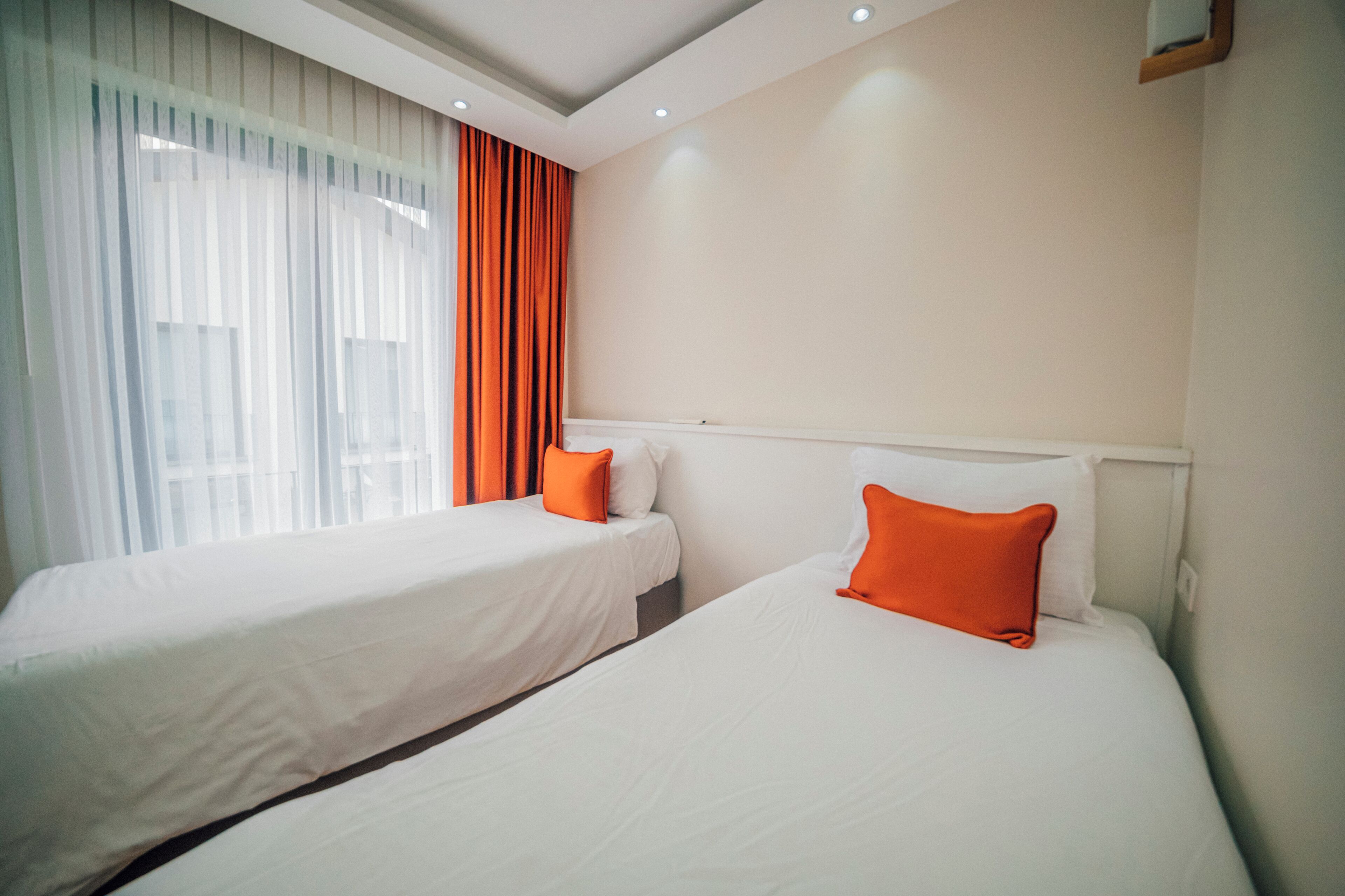 A hotel room with two beds, white bedding, and orange pillows.