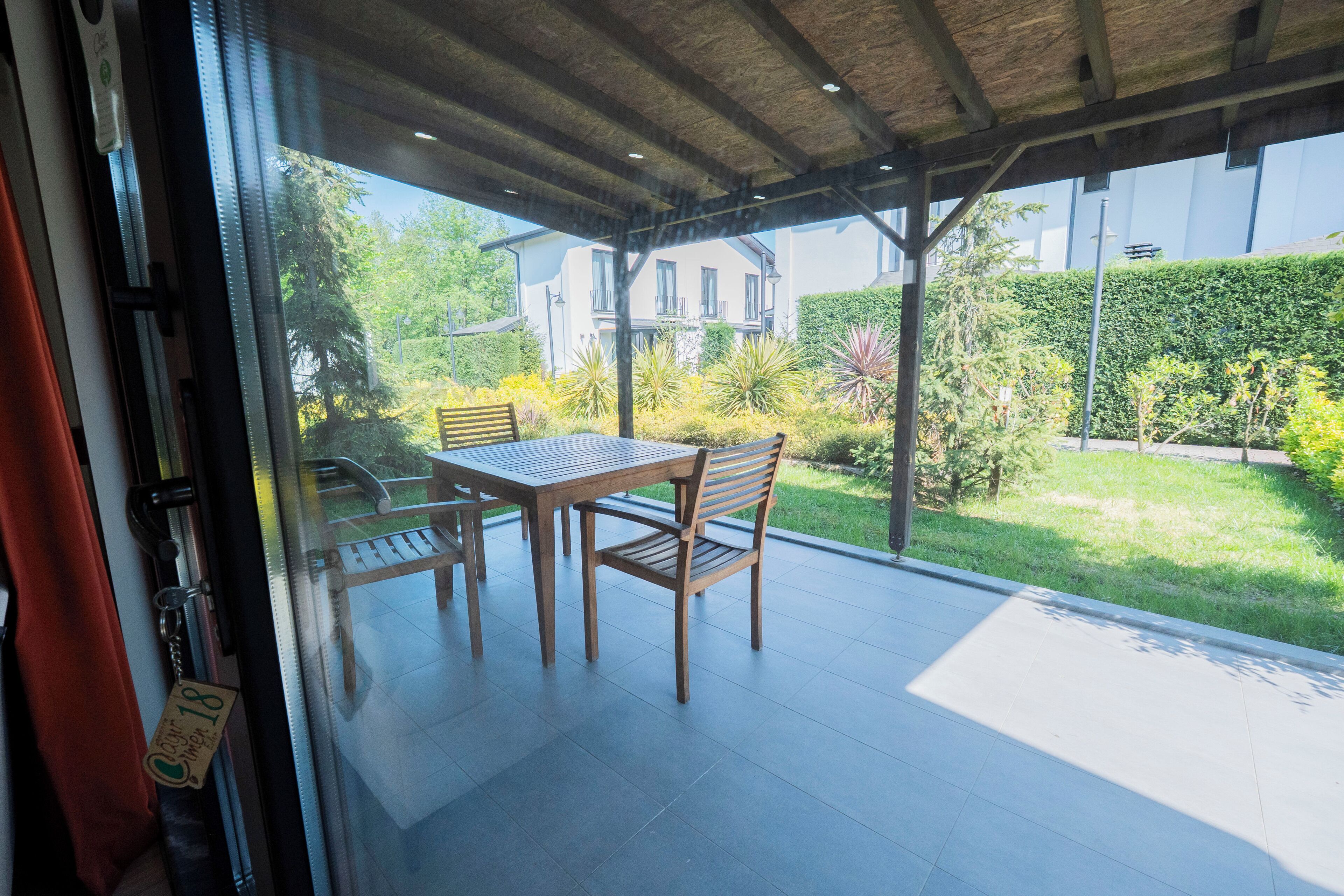 Une terrasse avec une table et des chaises, une porte vitrée et une vue sur une maison et un jardin.