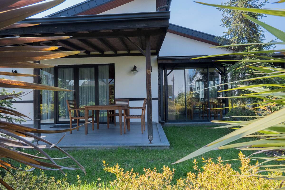 Een modern huis met een overdekt terras, een eethoek en een verzorgd gazon.