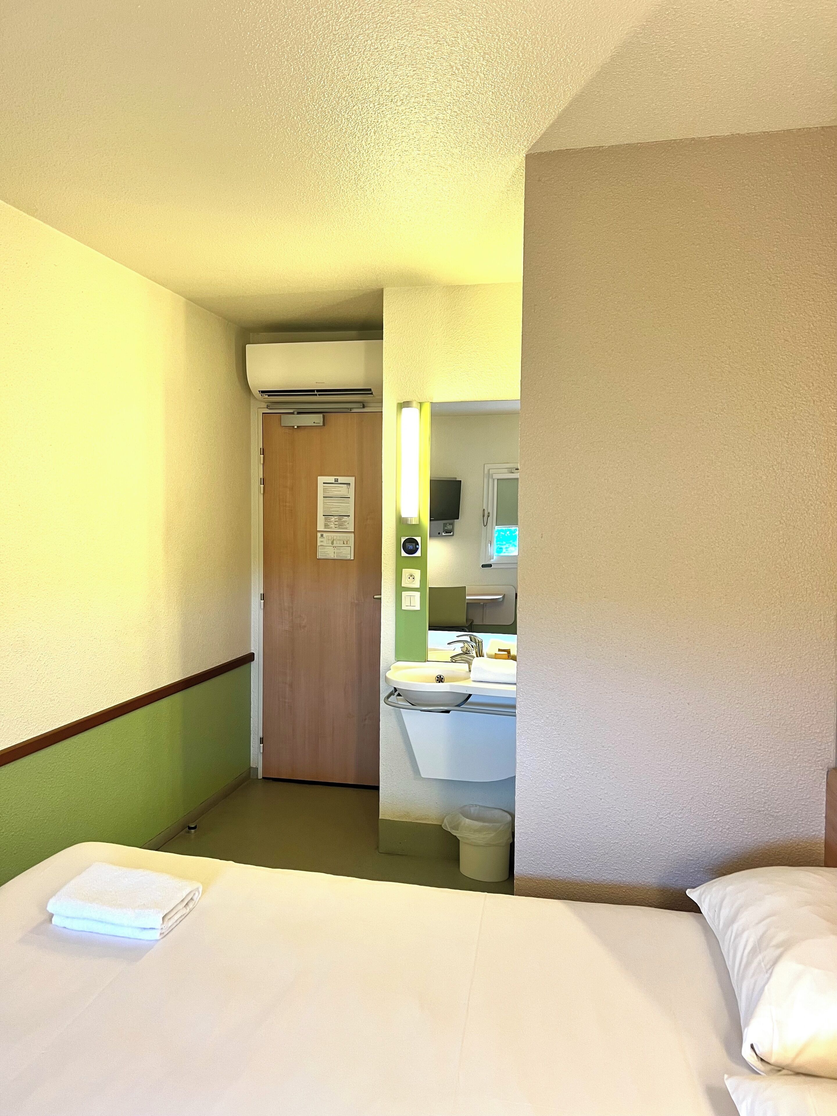 A hotel room with a bed, a bathroom with a sink and mirror, and a door leading to another room.