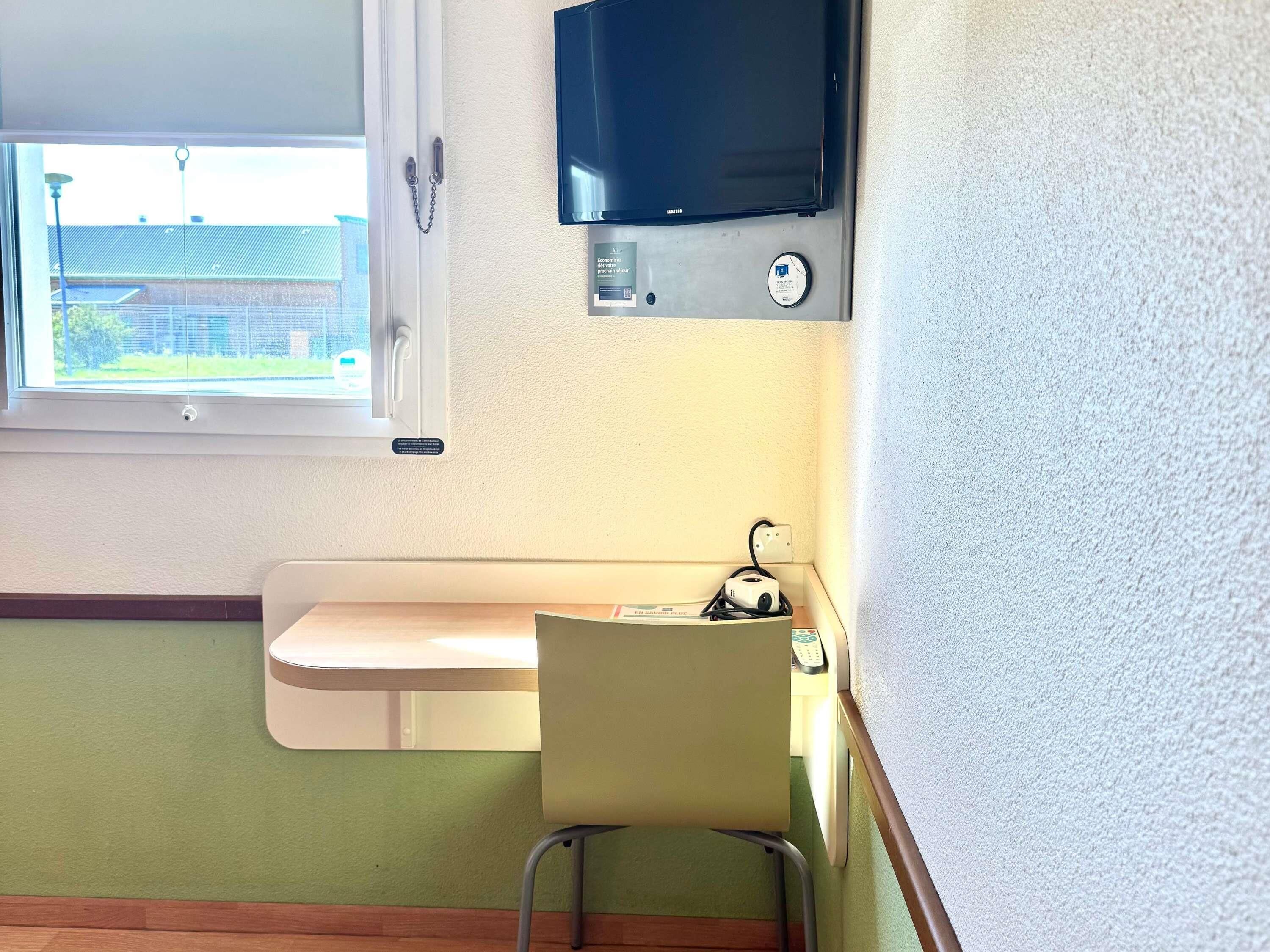 Una habitación pequeña con ventana, lavamanos, silla, televisor y termostato.