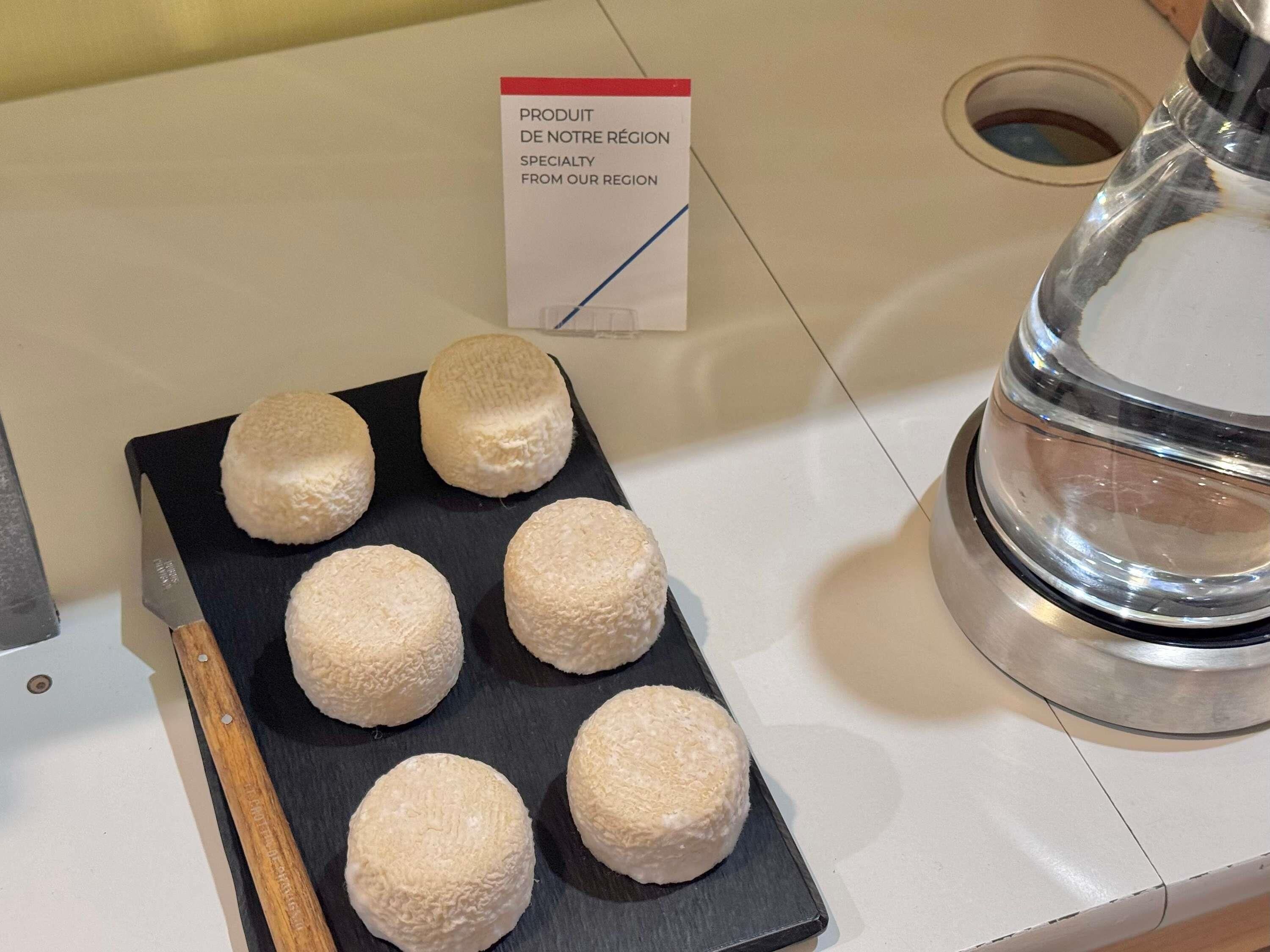 A tray of round, white pastries on a black slate, a sign indicating local specialty, and a stainless steel water dispenser.