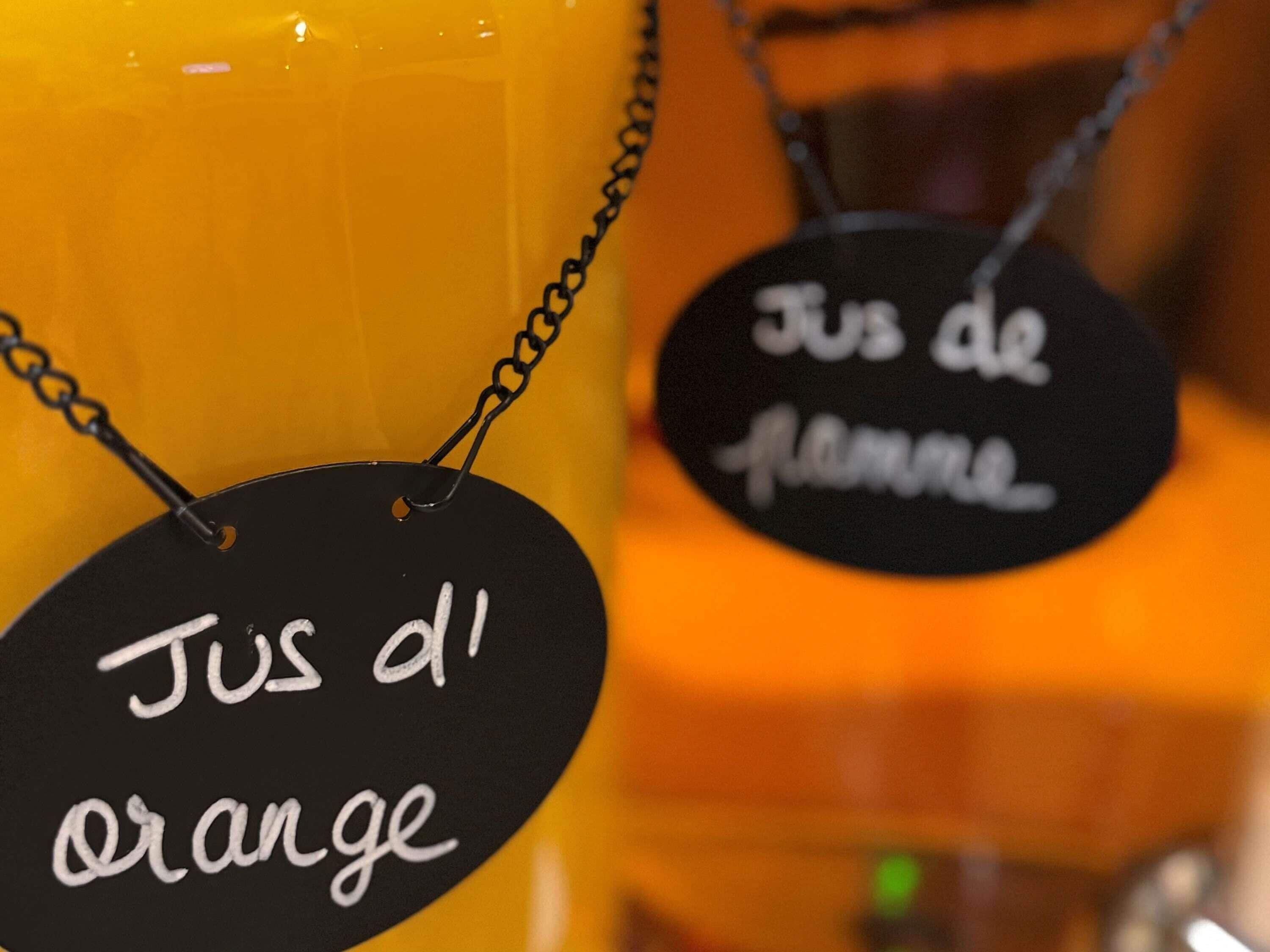 A close-up of a candle with a black tag labeled 'Jus d'orange' and another tag labeled 'Jus de flamme'.