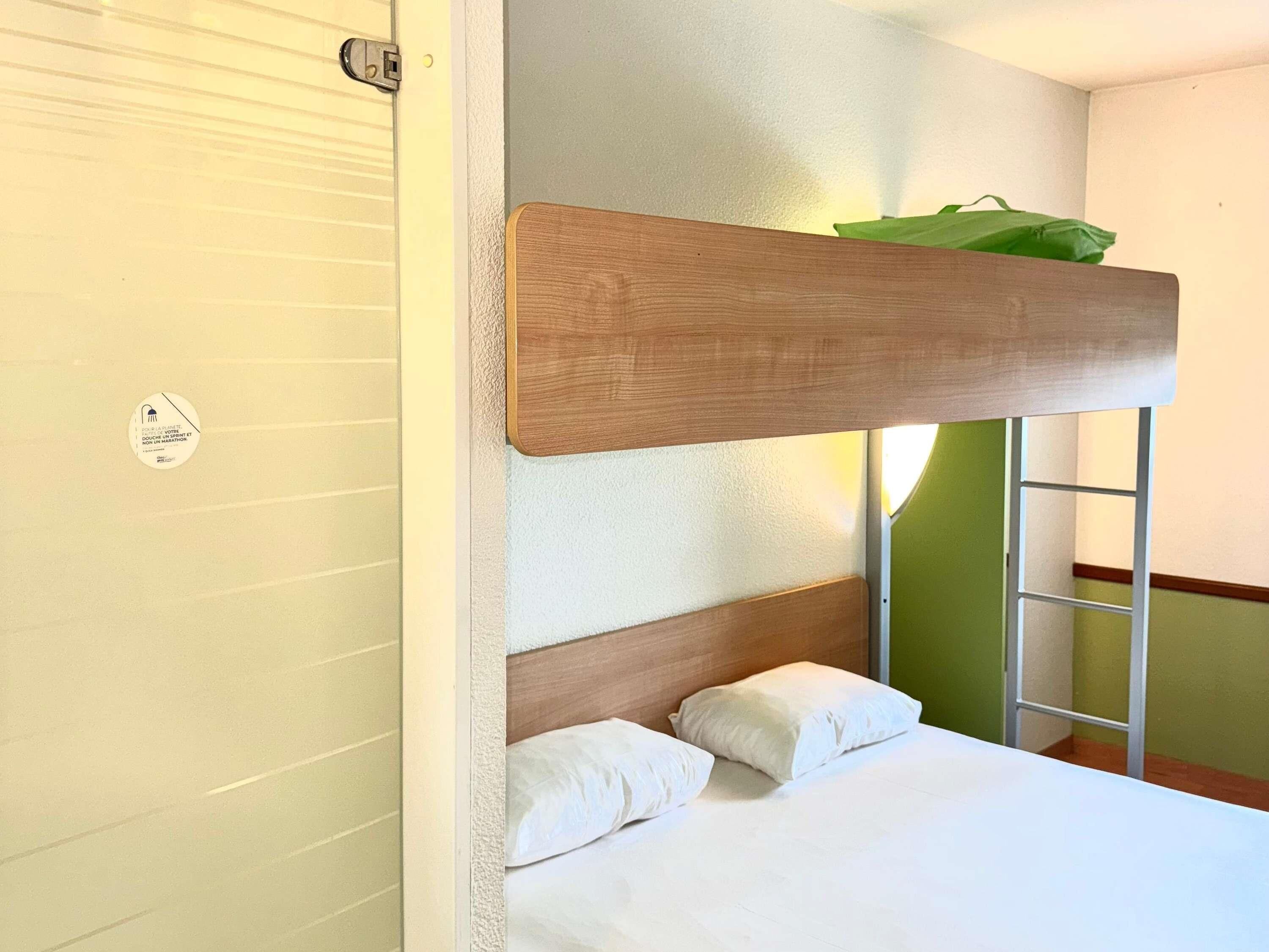 A bunk bed with a wooden headboard, white bedding, and a green wall.