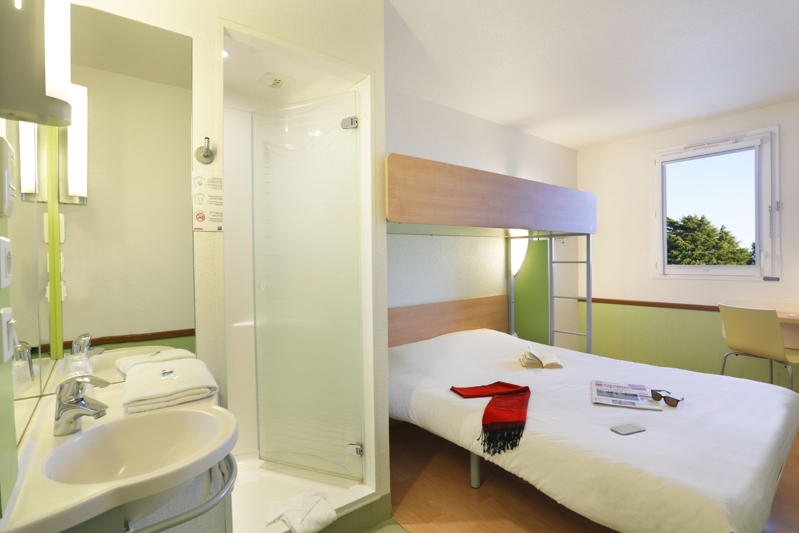A hotel room with a bathroom, a bed, a desk, and a window.